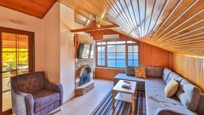 A cozy room with a fireplace, a sofa, a television, and a large window overlooking a scenic view. - Villa Dundar Kas Apartments (Kas)