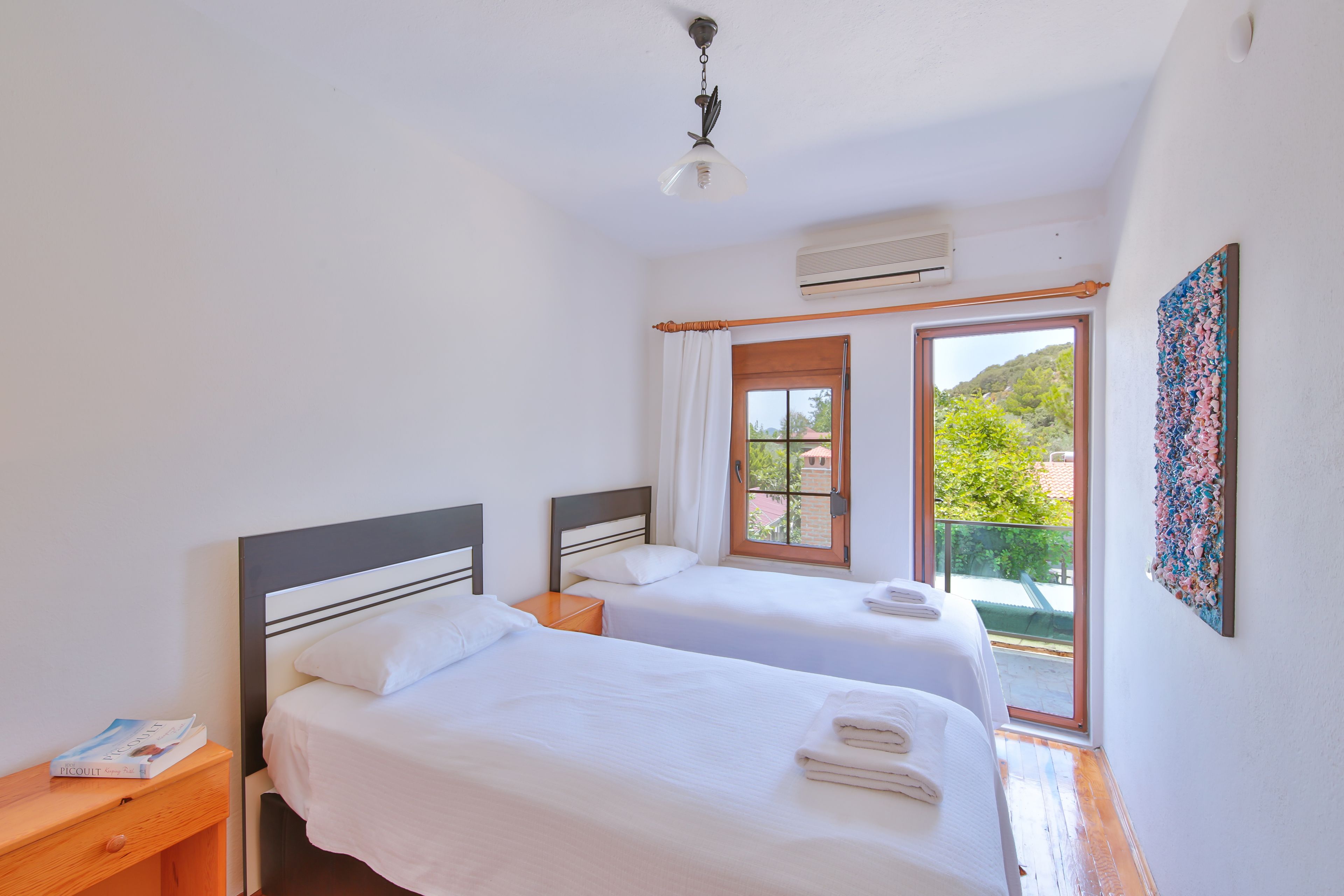 A bedroom with two beds, a window with curtains, a ceiling fan, and a wall-mounted air conditioner.