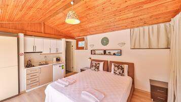A bedroom with a large bed, a wooden ceiling, a small kitchenette, and a bathroom.