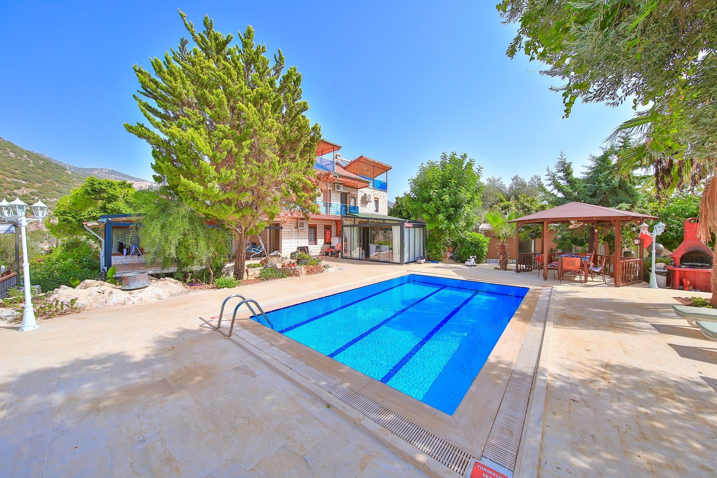 A swimming pool with a clear blue water, surrounded by a patio area with outdoor furniture and a gazebo.