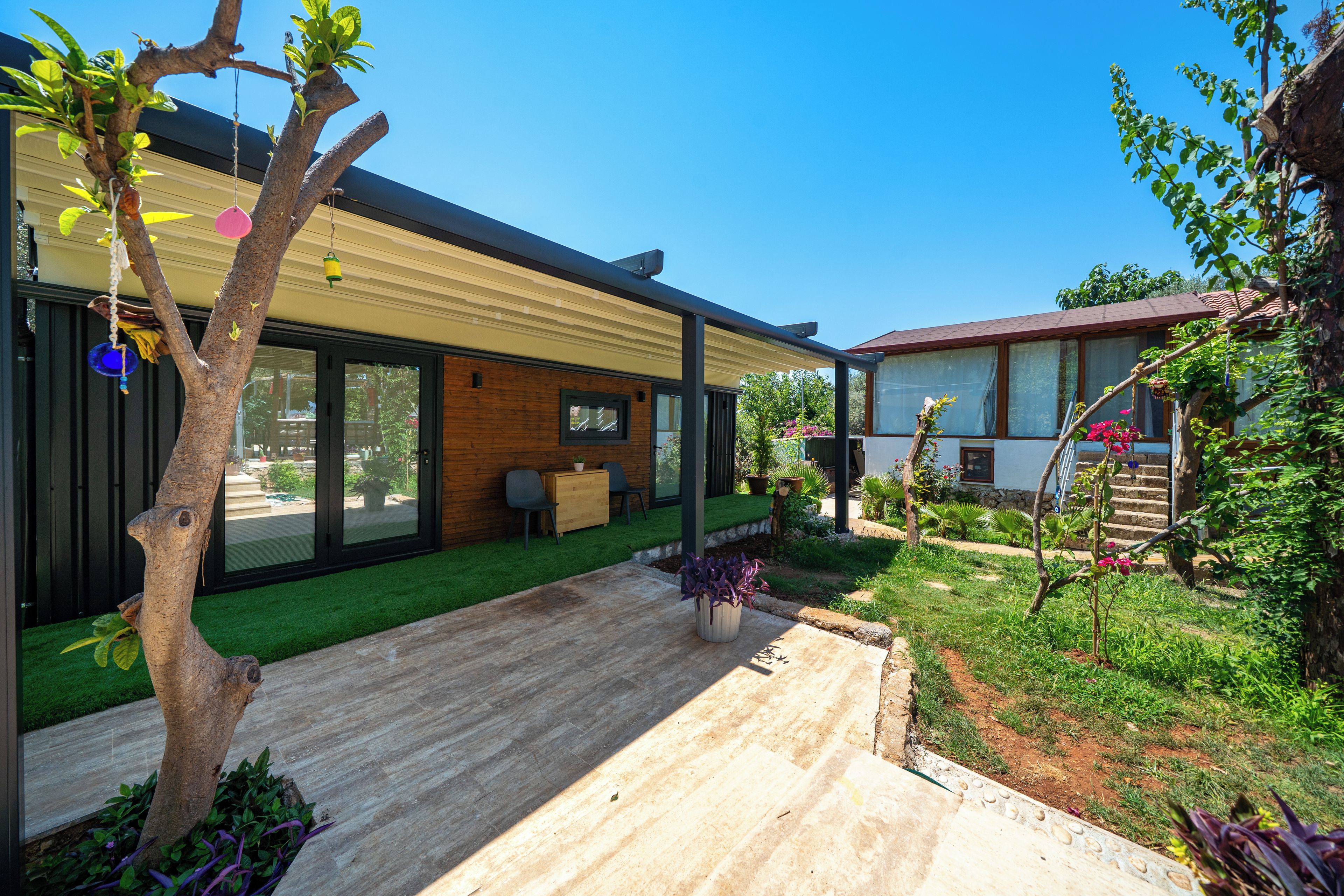 A modern house with a patio, a wooden deck, and a garden with various plants.