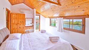 A bedroom with a wooden ceiling, a large bed with white linens, a wooden wardrobe, and a window with a view. - Villa Dundar Kas Apartments (Kas)