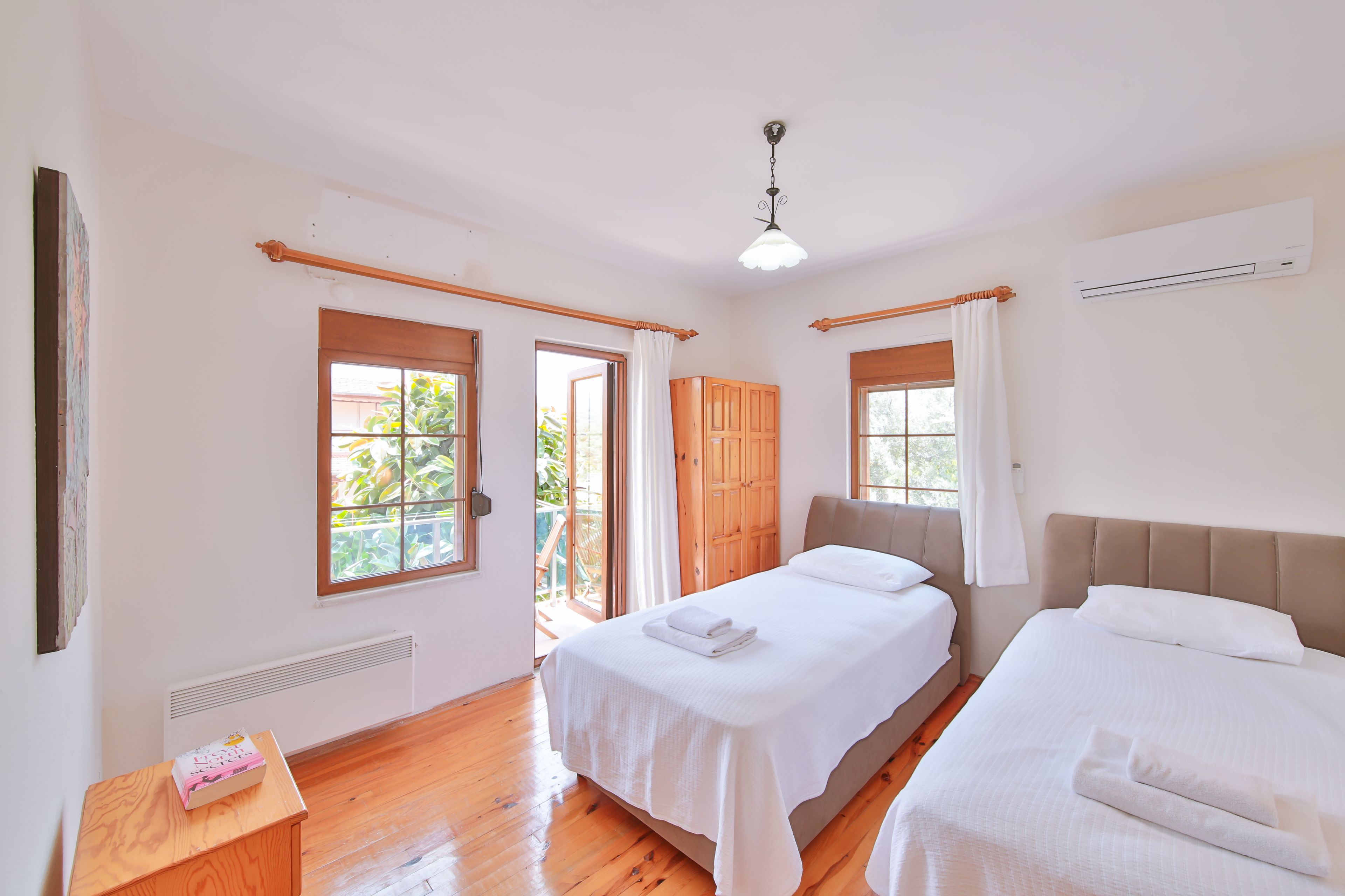 A bedroom with two beds, a wooden wardrobe, a small table with a box, and a ceiling fan.