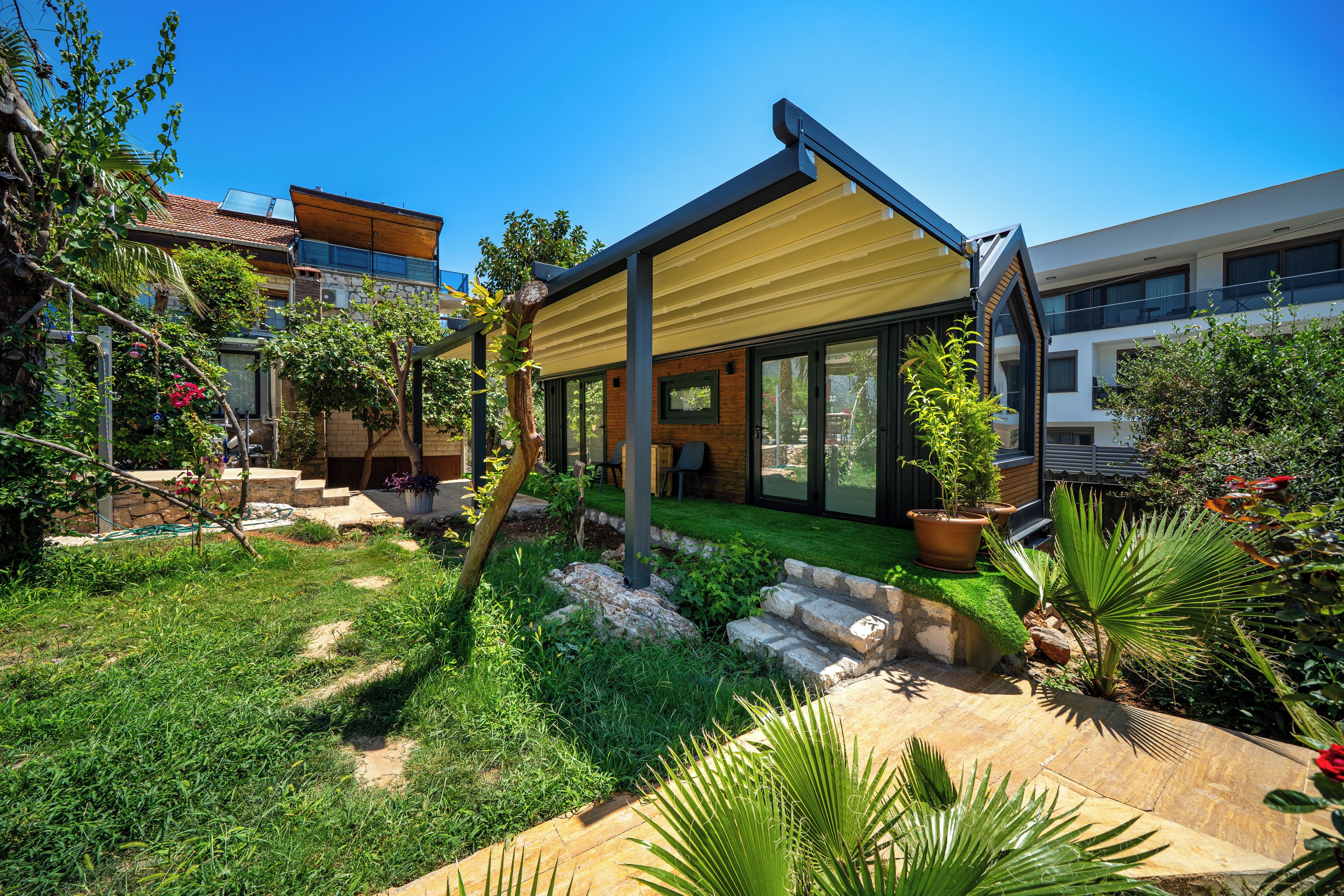 Une maison moderne dotée d’un patio, d’un jardin et offrant une vue sur les bâtiments voisins.