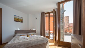 A bedroom with a large bed, a painting on the wall, and a view of the outside balcony.