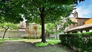 A courtyard with a large tree, a stone wall, and a building with a bell tower.