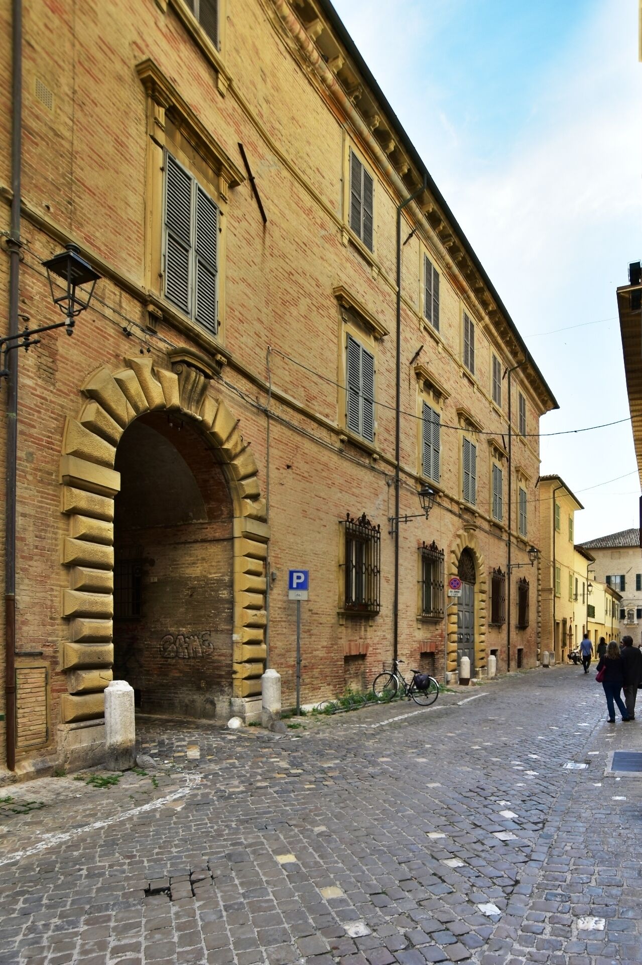 A historic building with a large arched entrance, a cobblestone street, and a blue parking sign.