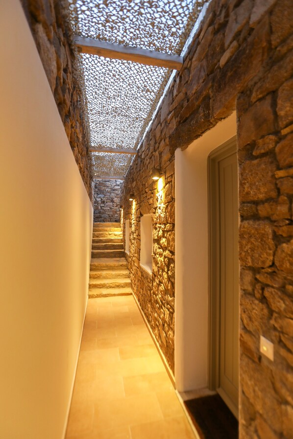 A stone-walled hallway with a tiled floor, a wooden door, and a ceiling with a patterned design.