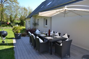 Ein Essbereich im Freien mit einem langen Tisch, Stühlen und einem großen Sonnenschirm.