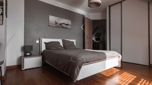 Een moderne slaapkamer met een houten vloer, een bed met een witte hoofdbord, een nachtkastje met een lamp en een schilderij aan de muur.
