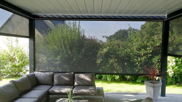 Een terras met een bank en bijzettafeltje, omgeven door glazen wanden met uitzicht op een tuin.