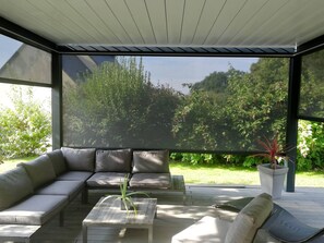 Un espace extérieur aménagé avec un canapé et une table basse, entouré de murs de verre donnant sur un jardin.
