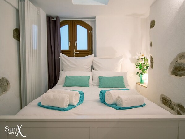 A neatly made bed with white and teal bedding, a wooden door in the background, and a stone wall. - Charming 3-bed, 3-bath house in old Antibes with terrace & aircon. Parking close (Antibes)
