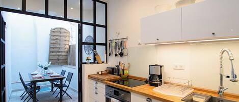 Una cocina compacta con encimera de madera, horno empotrado y fregadero. Se ve un área de comedor con una mesa y sillas a través de una puerta abierta.