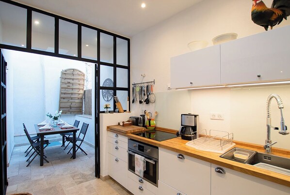 A compact kitchen with a wooden countertop, a built-in oven, and a sink. There is a dining area with a table and chairs visible through an open door.
