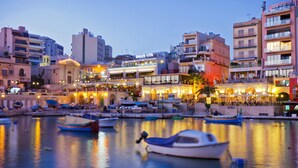 A waterfront area with boats docked, a building with a sign reading "DOLCE VITA", and a variety of other buildings in the background. - SEAFRONT LUXURY APT WITH POOL (Sliema)