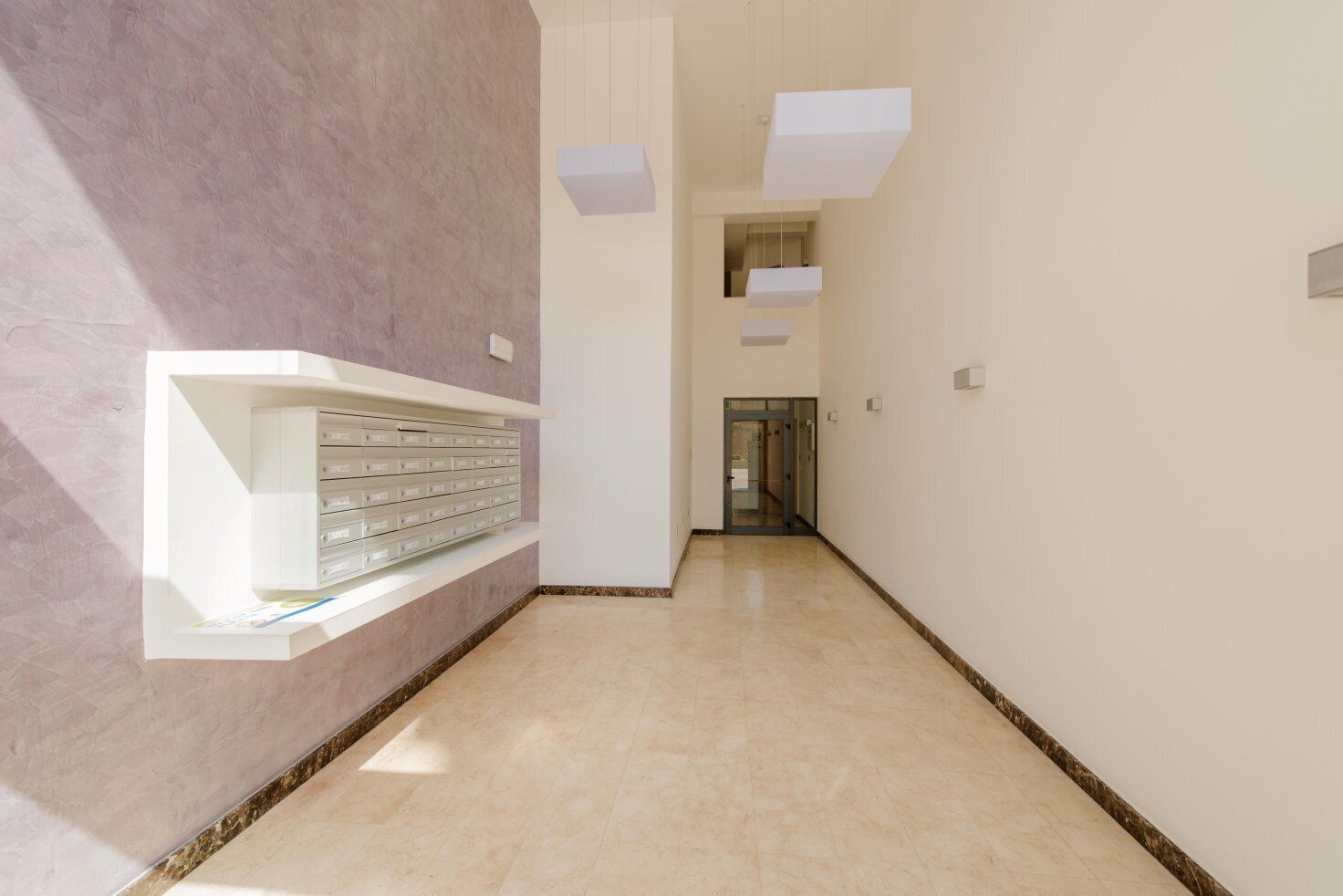 A modern hallway with a marble floor, white walls, and a built-in storage unit on the left.