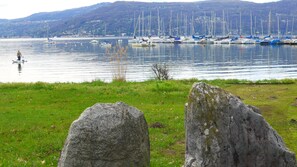 Un port de plaisance avec des bateaux amarrés, un premier plan verdoyant parsemé de gros rochers et, au loin, un paysage vallonné.