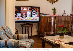 Een woonkamer met een televisie waarop game titels staan, een bank, een houten kast en een potplant.