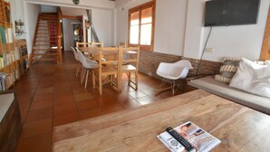 Un'ampia zona giorno con una scala in legno, un tavolo da pranzo con sedie, un divano e una televisione a parete.