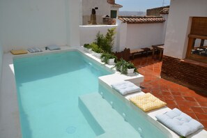 Ein rechteckiger Swimmingpool mit weißen Stufen, umgeben von Blumentöpfen und Gartenmöbeln.