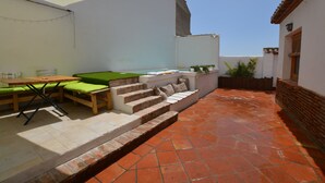 Un patio con tavolo e sedie, una piccola scala e un muro bianco con una finestra.
