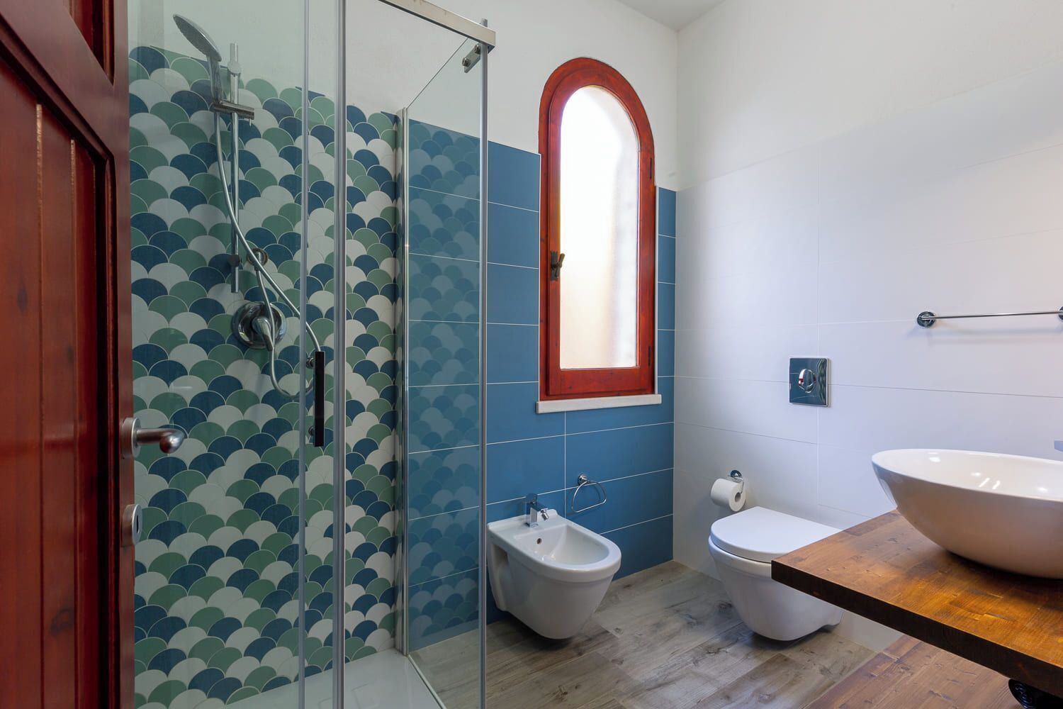 A bathroom with a glass shower enclosure, a bidet, a toilet, and a large sink.
