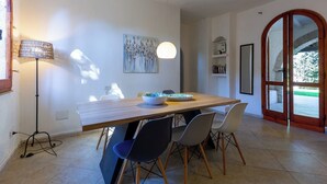 Een eetgedeelte met een houten tafel, stoelen, een vloerlamp en een schilderij aan de muur.