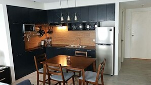 A modern kitchen with dark cabinetry, a stainless steel refrigerator, and a wooden dining table with chairs. - BACOLOD CITY CENTER  SLEEK STUDIO DE LUXE (Bacolod)