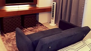 A modern living room with a flat-screen TV mounted on a wooden wall, a standing heater, a dark sofa, and a patterned rug. - BACOLOD CITY CENTER  SLEEK STUDIO DE LUXE (Bacolod)