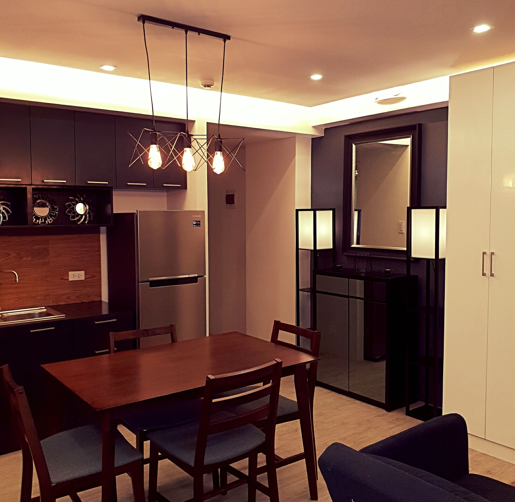 A modern kitchen with dark cabinets, a built-in refrigerator, and a dining area with a wooden table and chairs.