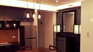 A modern kitchen with dark cabinets, a built-in refrigerator, and a dining area with a wooden table and chairs. - BACOLOD CITY CENTER  SLEEK STUDIO DE LUXE (Bacolod)