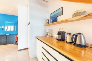 A modern kitchen with a wooden countertop, a coffee maker, a kettle, and a shelf with books and a hat. - Balcone di Noa e Stella, Menaggio, Italy (Menaggio)