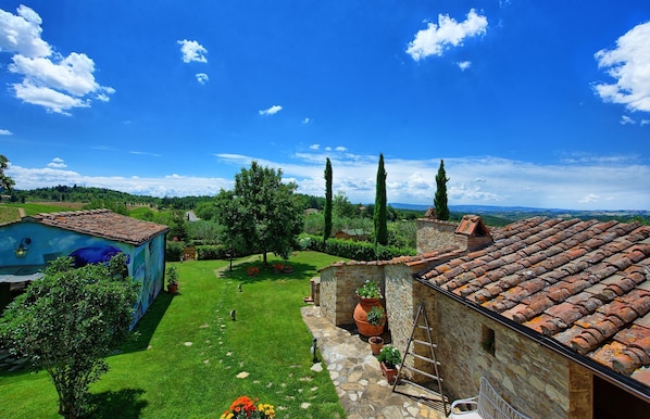 A courtyard with a stone wall, a tiled roof, and a grassy area with potted plants.