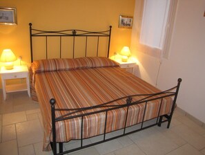 Ein Einzelbett mit gestreifter Bettdecke, zwei Nachttische mit Lampen sowie eine schlichte Wand mit einem Bilderrahmen.
