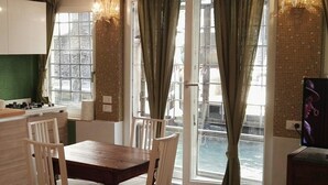 Un coin repas avec une table et des chaises en bois, une cuisine avec un plan de travail vert et de grandes fenêtres avec des rideaux.