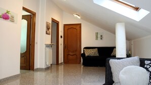 Un'ampia zona giorno con soffitto alto, un lucernario, una porta in legno e un divano nero con cuscini decorati.