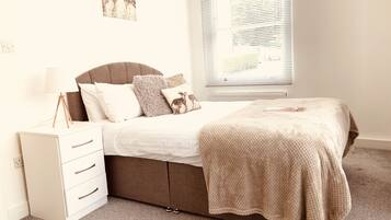 A bedroom with a bed, a bedside table, a lamp, a dresser, and a window with blinds.