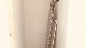A small, narrow room with a white door, a radiator, and a hanging clothes rack.