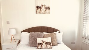 A bedroom with a bed, white bedding, a headboard, a nightstand with a lamp, and a wall-mounted artwork of deer.