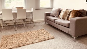 A modern living room with a grey sofa, white chairs, a beige rug, and a decorative wall piece.