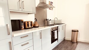 A modern kitchen with white cabinets, a stainless steel range hood, a kettle, and a trash can.