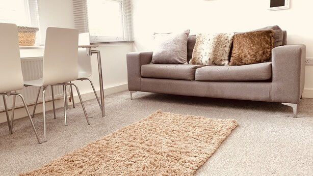 A modern living room with a grey sofa, white chairs, and a beige rug.