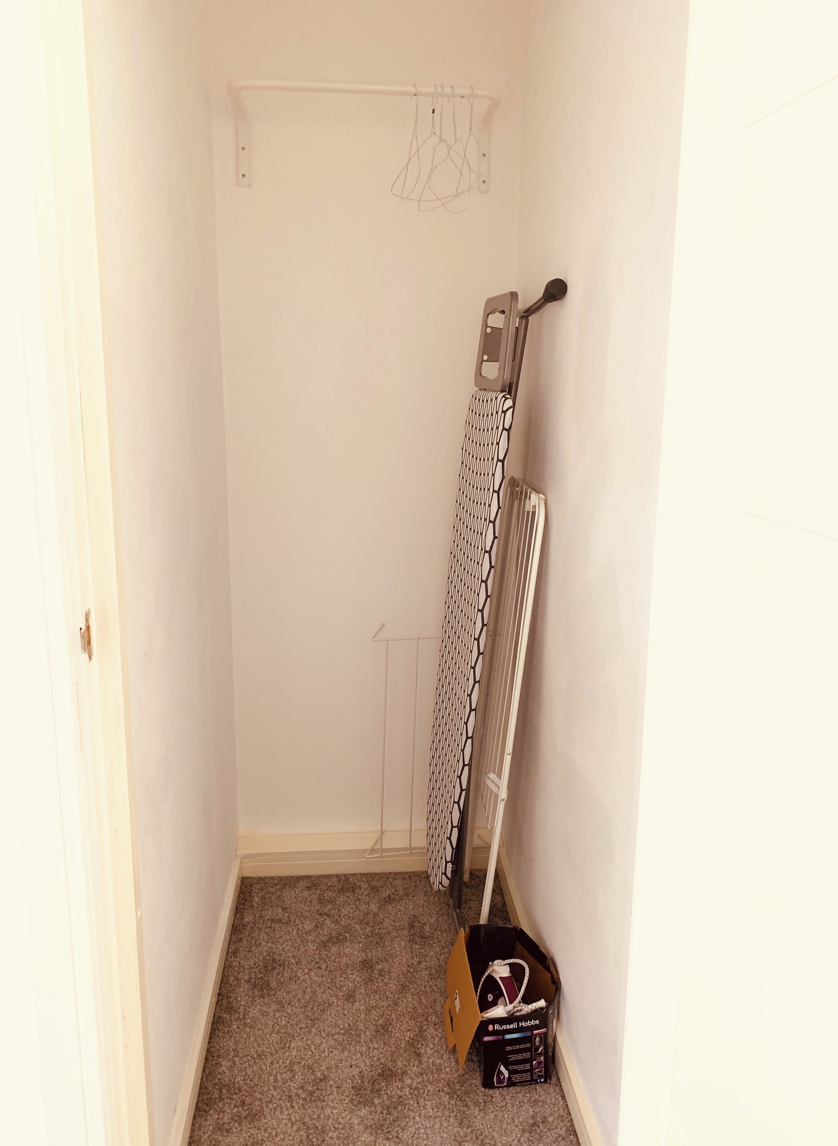 A small, narrow room with a white door, a radiator, and a hanging clothes rack.