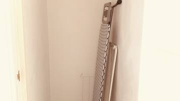 A small, narrow room with a white door, a radiator, and a hanging clothes rack.