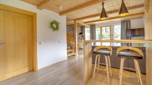 Ein Holzinnenraum mit einer Treppe, einer Bar mit Hockern und einem an der Wand befestigten Fernseher.