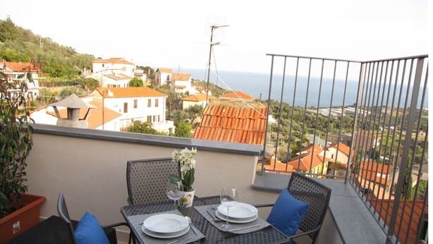 Un balcon avec une table dressée pour deux personnes, donnant sur une ville côtière.