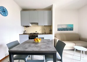 A modern kitchen with grey cabinets, a dining table with chairs, a bowl of fruit, and a sofa in a living area. - REGINA LAKE COMO, lake view (Dongo)