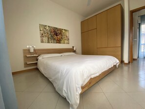 Quarto com cama, cabeceira de madeira, prateleira na parede e guarda-roupa espaçoso.
