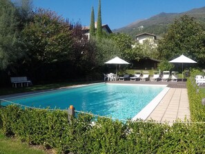 A swimming pool with lounge chairs and umbrellas, surrounded by greenery and a mountain backdrop. - REGINA LAKE COMO, lake view (Dongo)